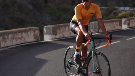 A-man-in-a-yellow-t-shirt-and-helmet,-seated-on-a-bicycle,-gazes-into-the-distance-while-positioned-on-a-mountain-road