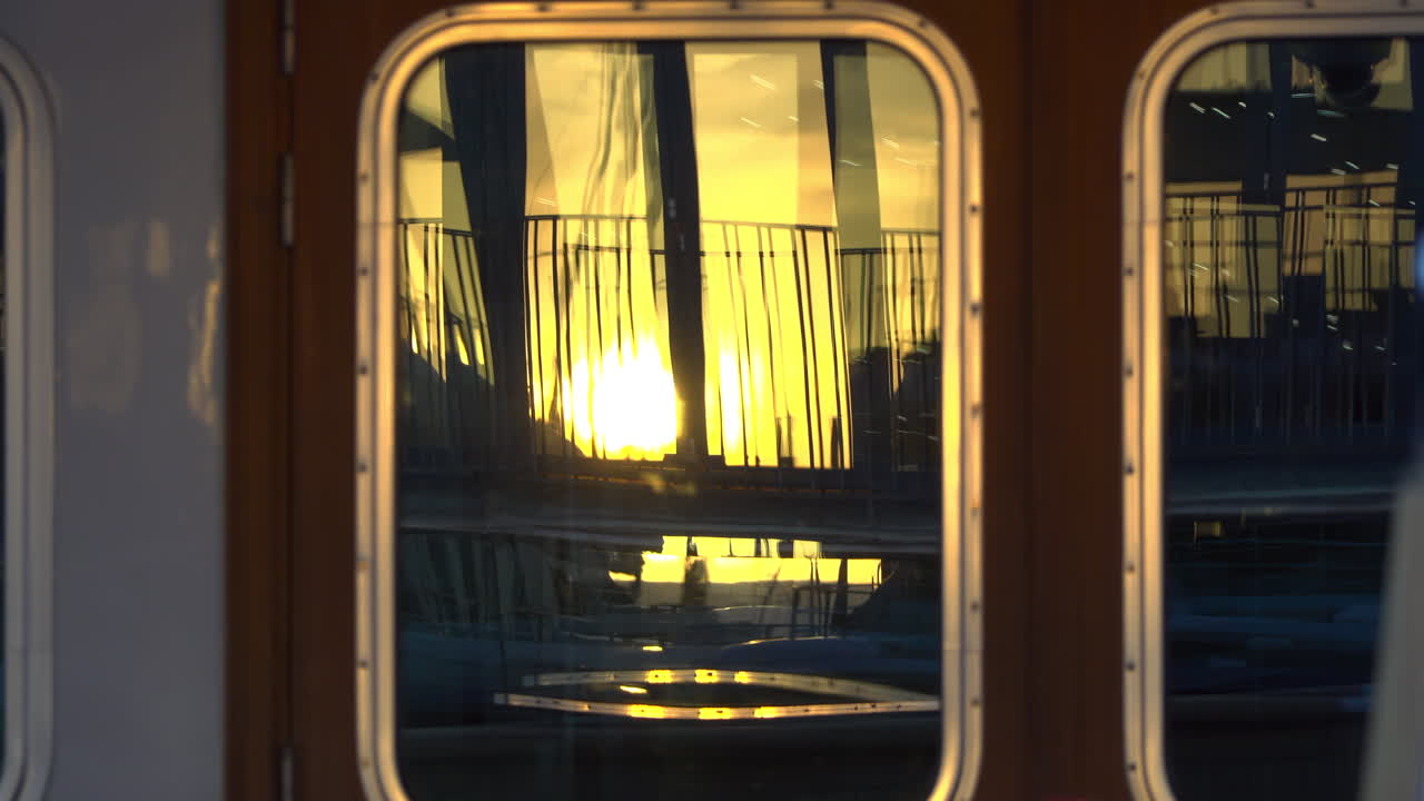Close-up of a yacht's window reflecting the golden sunset and marina railings in Cannes