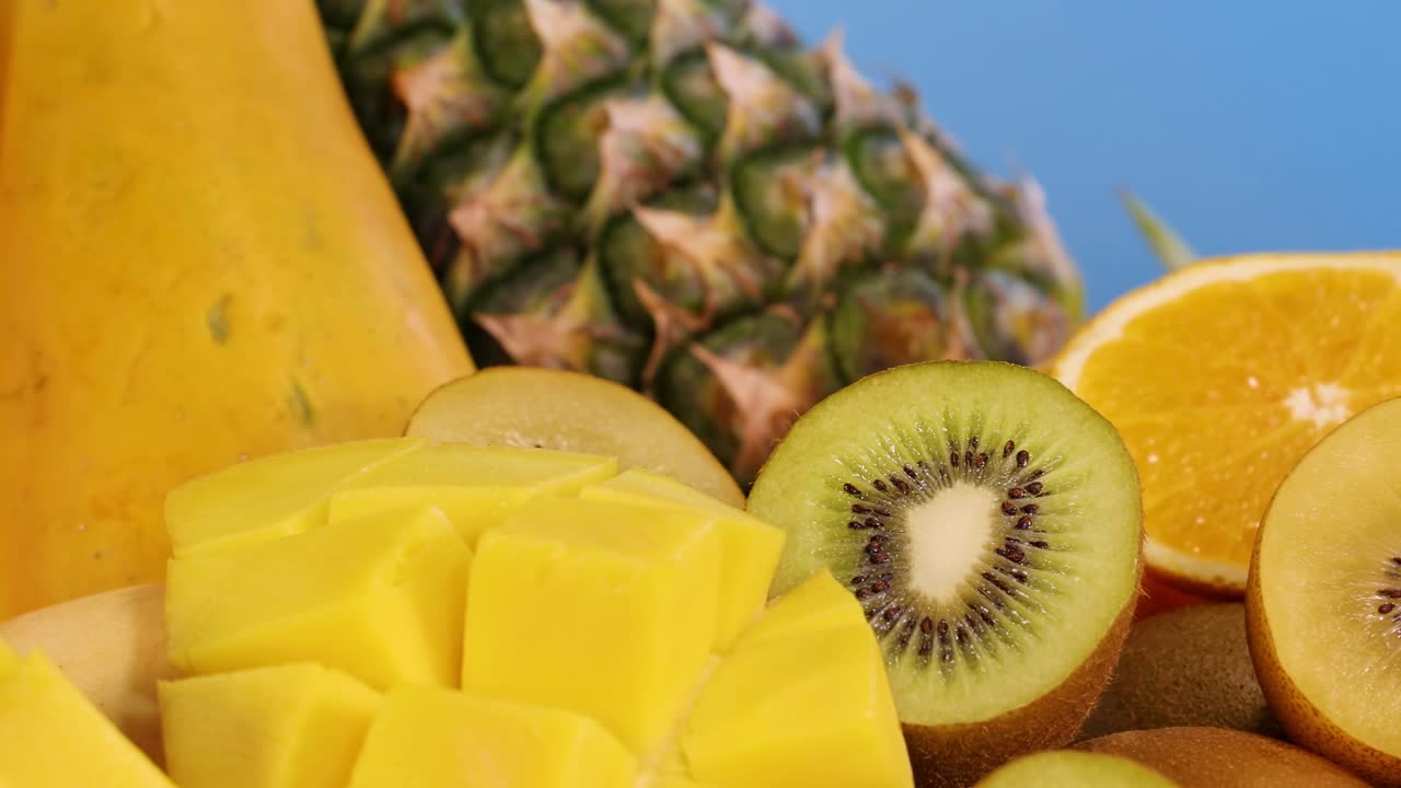 A colorful assortment of tropical fruits including papaya, pineapple, and pomegranate against a vivid blue backdrop.