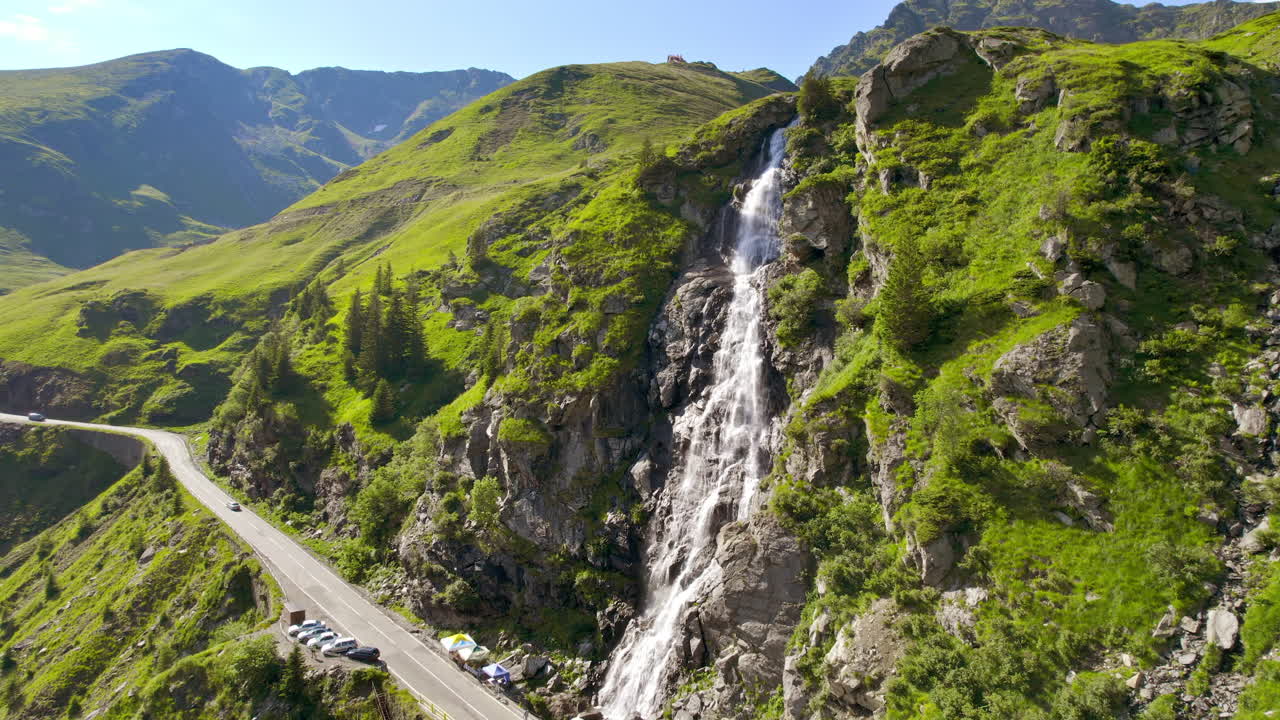Vista aerea con drone della natura in Romania. Strada Transfăgărășan sui Monti Carpazi con cascata vicino alla strada, pendii rocciosi con vegetazione