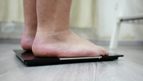 male feet stepping on bathroom weighing scale, close up