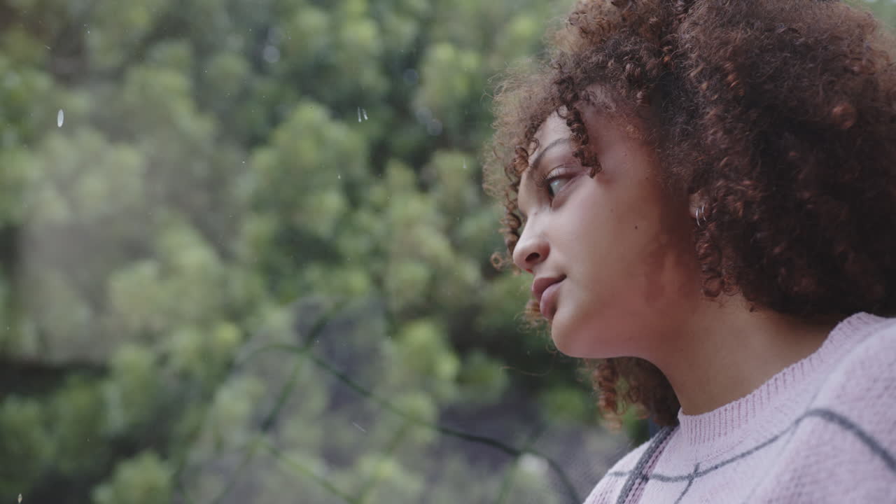 Looking out window, woman with curly hair reflecting on nature outside, copy space