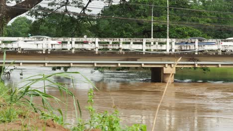 flowing muddy river under a bridge with assorted traffic