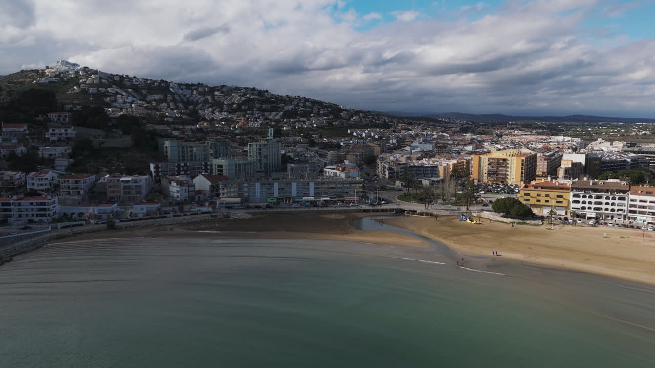 Drone tracks along beach near town of Peniscola with cloudy sky and empty shoreline