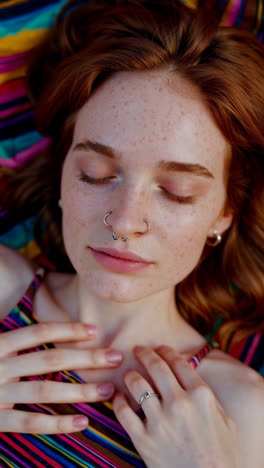 close-up portrait of a relaxed young woman with red hair, freckles, and piercings