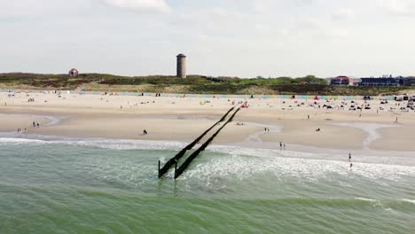 large lighthouse next to a beach in the netherlands crowded by many people