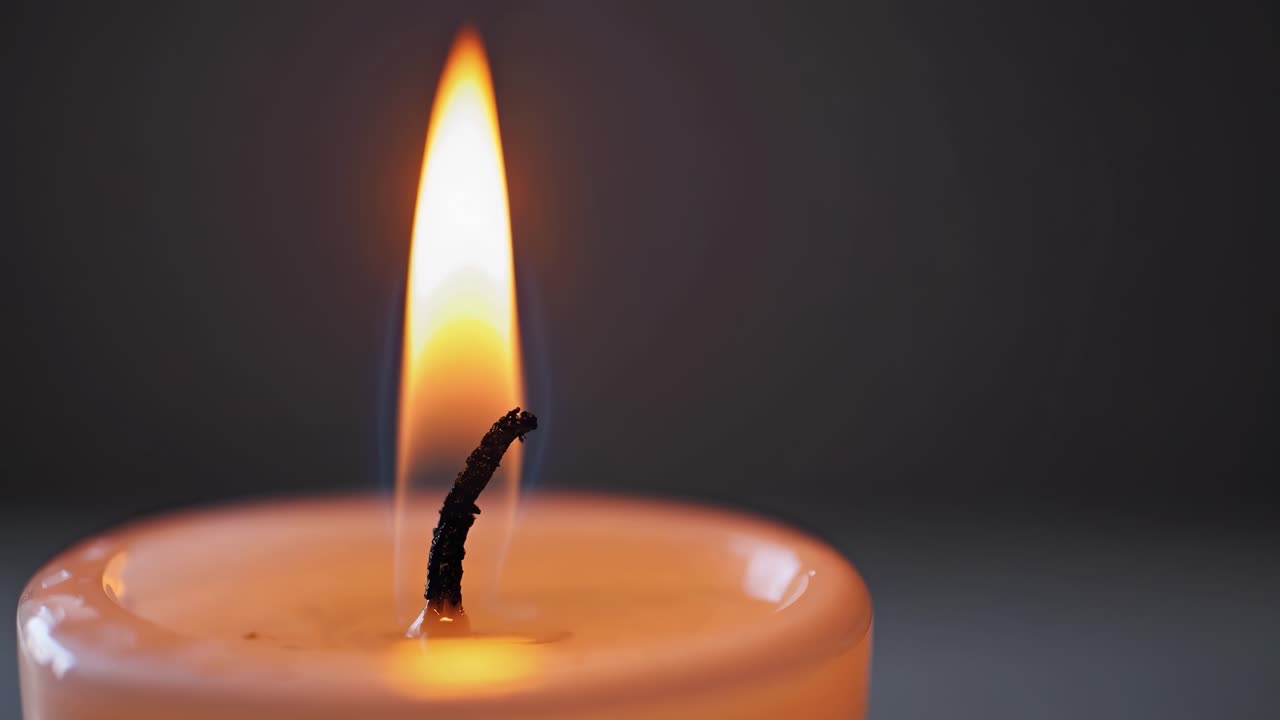 Close-up video of a candle flame, shot from a low angle. The soft glow creates a warm, serene