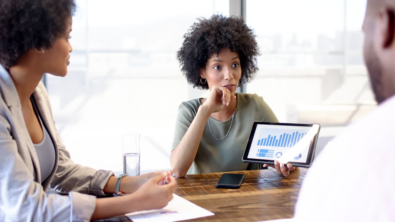African American woman showing tablet with graphs to diverse colleagues