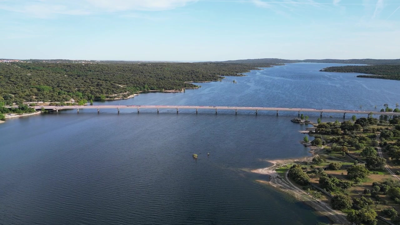 Most se táhne přes rozlehlé jezero obklopené hustými lesy pod jasnou oblohou. Ideální pro přírodopisné dokumenty nebo cestovatelský obsah
