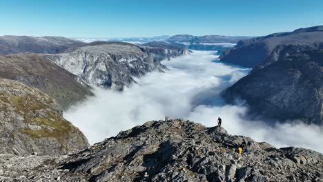 drone orbits from above, showing a couple and other tourists at the cliff edge of bakkanosi with stunning views of the fjord and fog below