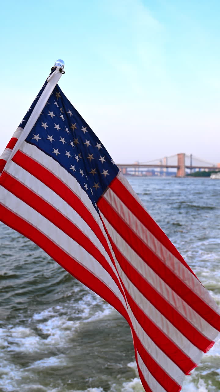 American flag on boat with Brooklyn Bridge in background. Close up of US flag waving on a boat moving through East River New York