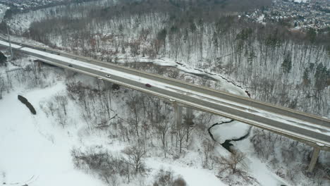 aerial push in on a bridge as commuters drive down a snowy road in winter time