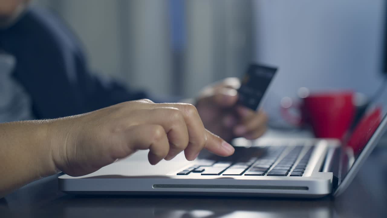 b rodar el movimiento lento de la mano escribiendo el teclado y haciendo compras en línea mientras sostiene la tarjeta de crédito. el titular de la tarjeta sostiene la carta de crédito haciendo pago en línea de e-bank. pagar por la compra en la tienda web usando una computadora portátil