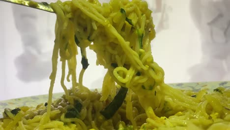 primer plano de fideos instantáneos con vegetales verdes levantados con la ayuda de un tenedor de metal antes de comer