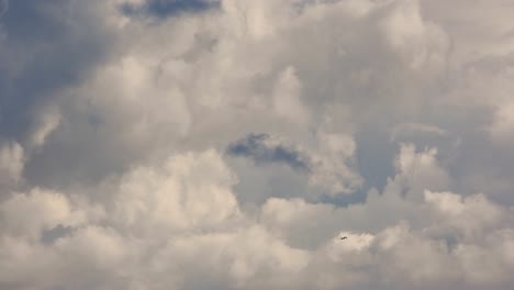 Stationary-shot-of-a-cloudy-clear-blue-sky-while-an-airplane-is-passing-by-the-frame