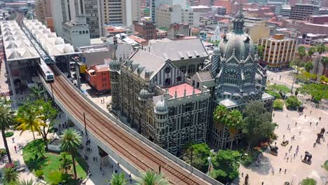 stunning aerial 4k shot of plaza botero and moving metro train on railway surrounded with palms