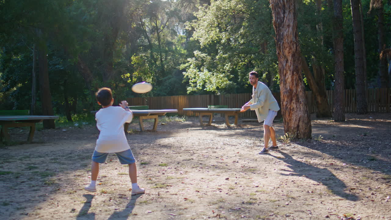 Carefree family playing outdoor game on playground. Boy throwing plate to father