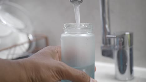 filling a glass bottle with water from a faucet