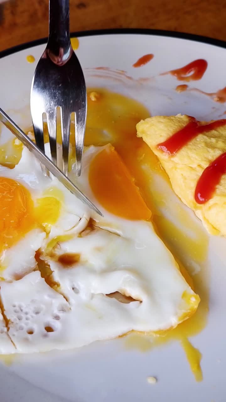 Un primo piano verticale che mostra una forchetta e un coltello che tagliano le uova con ketchup