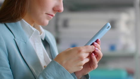 Close-up: a Young woman in a suit designer business woman in a tailoring Studio with a mobile phone in a sewing workshop writing messages to customers. Writing a text message in the office.