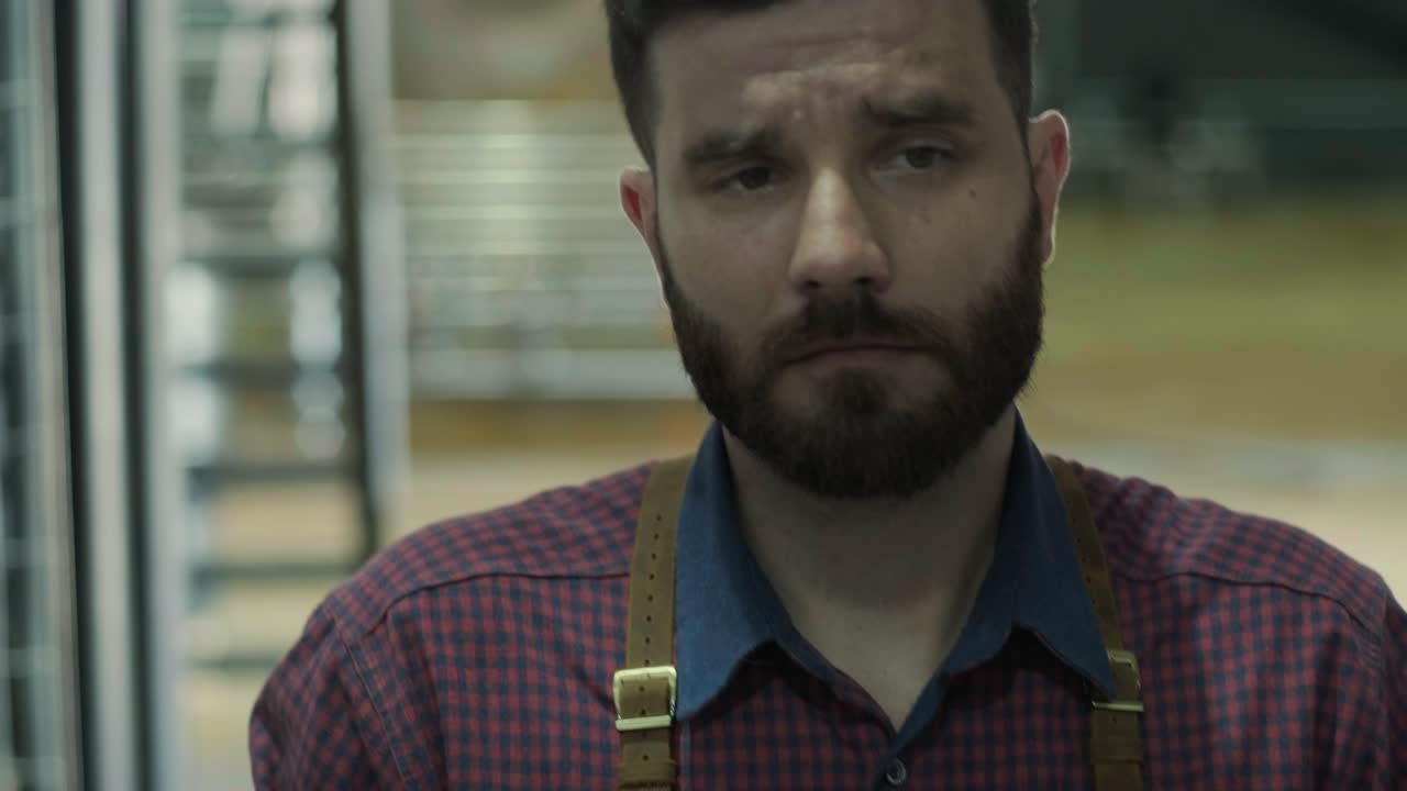 Young brewer wearing a leather apron carries a barrel of craft beer at a modern brewery