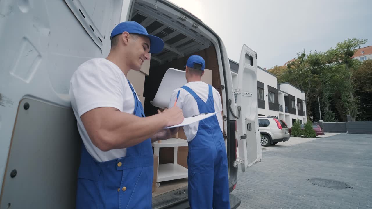 dos jóvenes trabajadores de una compañía de mudanzas están cargando cajas y muebles en un minibus