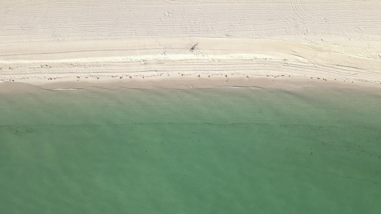 vista aérea: la persona se sienta sola en la playa de arena, suaves olas verdes