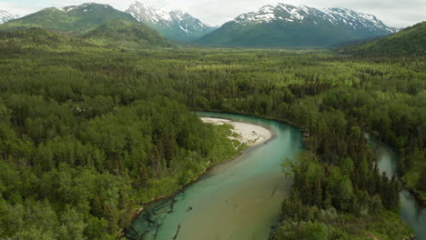 Beautiful-aerial-pan-up-from-winding-green-river-in-the-wilderness-of-Alaska-to-mountains-in-the-background