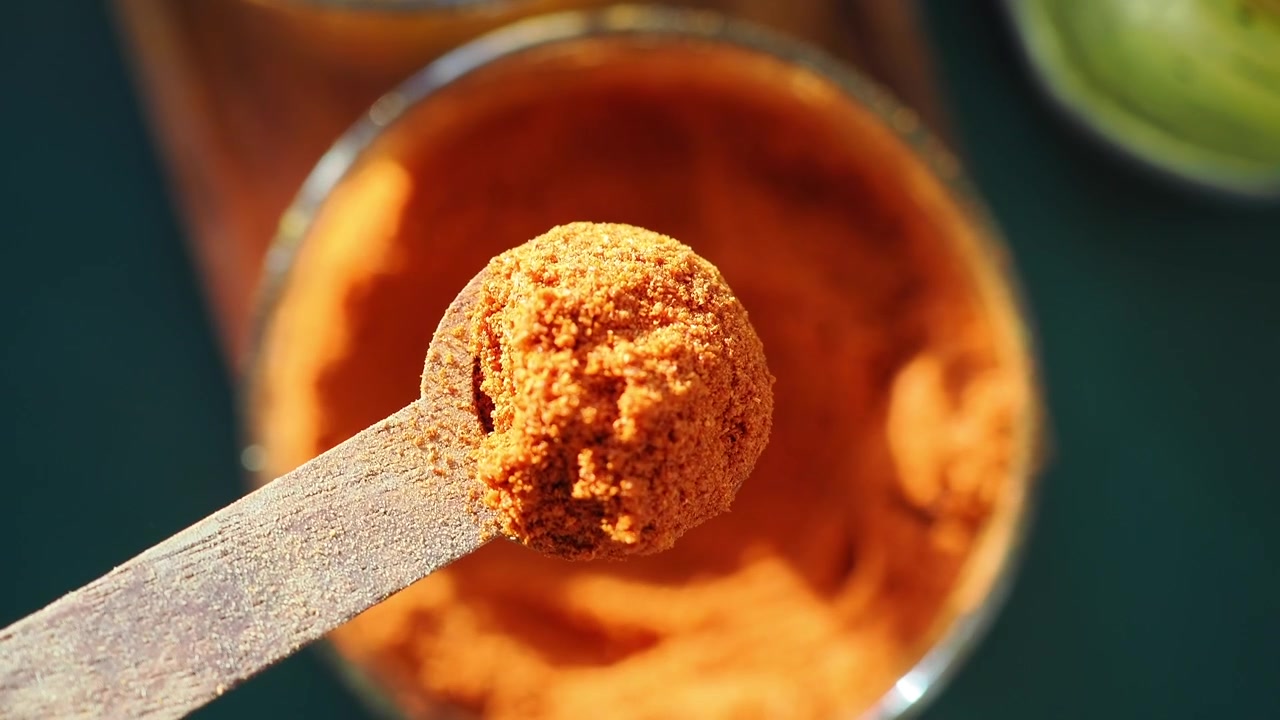 Wooden Spoon Scooping Orange Spice Powder from Glass Jar