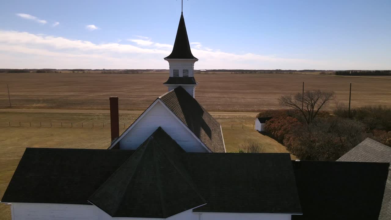 180 degree aerial orbit around an old church in Alberta, Canada. 4k footage of a white abandoned country chapel made of wood in the early 20th century. Person standing in front of the building