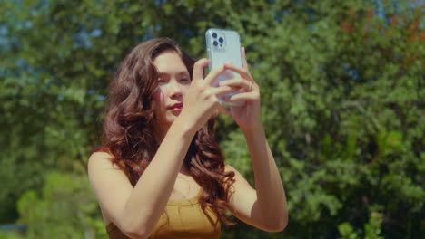 una mujer filmando la naturaleza del parque en primer plano, una morena asiática haciendo paisajes fotográficos.