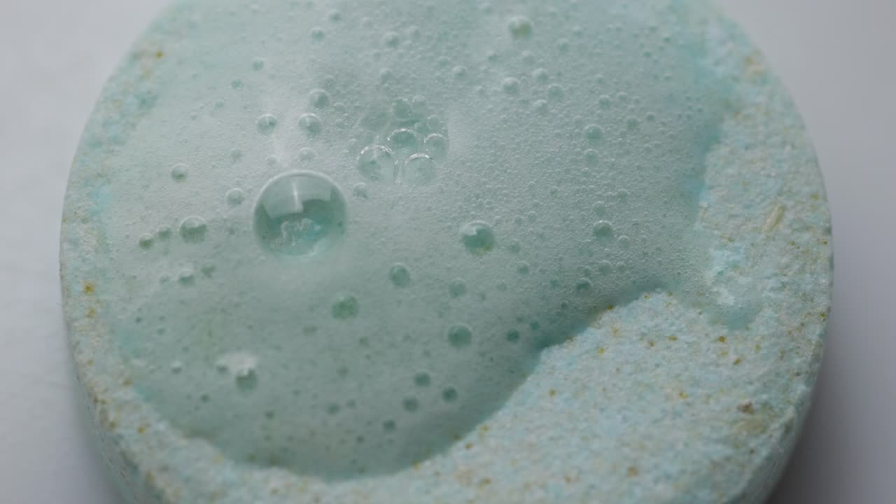 Overhead Macro Shot Of An Effervescent Tablet Fizzing With Bubbles (Chemical Reaction) When Water Droplets Touch The Surface.