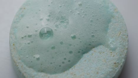 overhead macro shot of an effervescent tablet fizzing with bubbles (chemical reaction) when water droplets touch the surface.