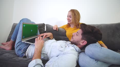 una pareja enamorada en un sofá mirando una computadora portátil. un niño tendido en el regazo de una niña. pantalla verde.