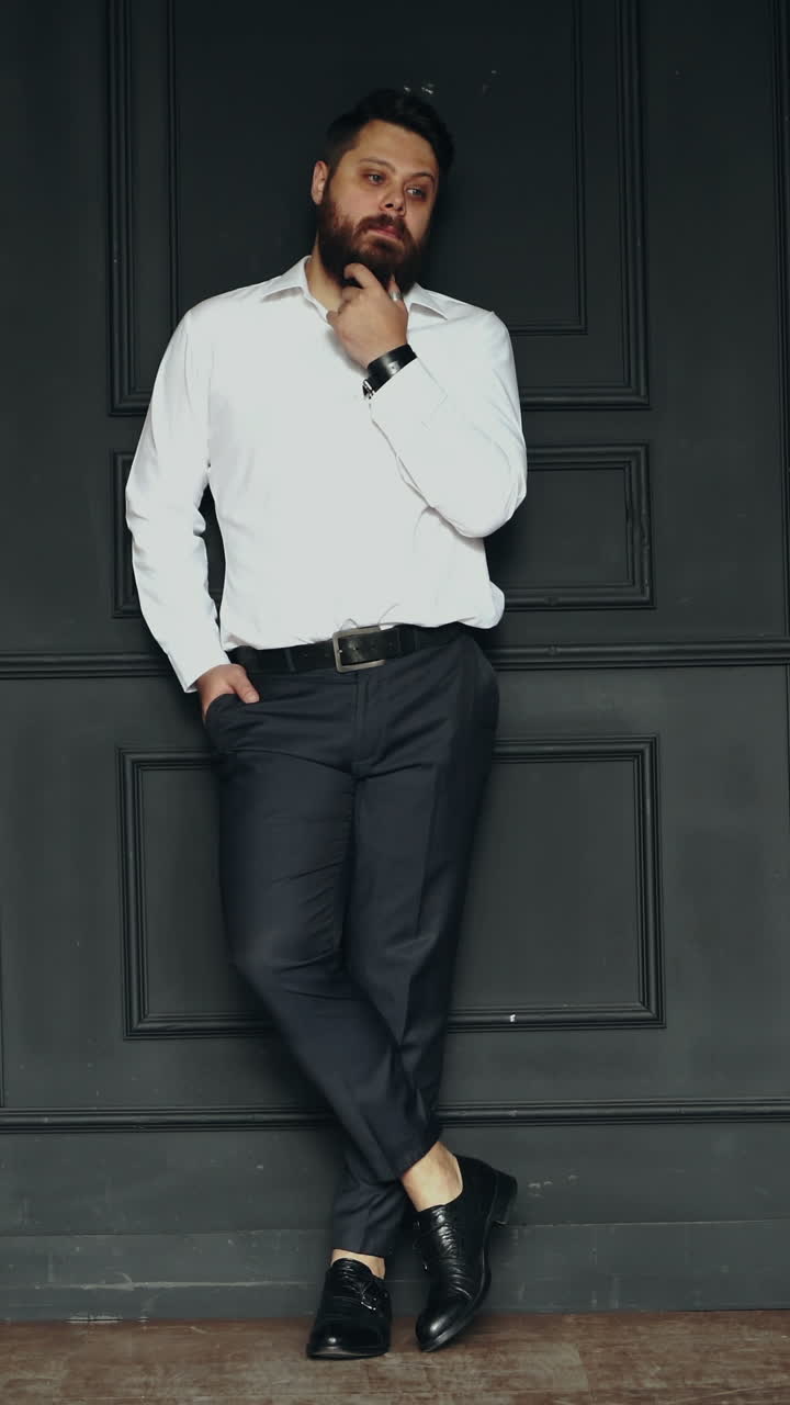 Serious man in studio. Stylish handsome young bearded man in white shirt posing in studio Vertical video