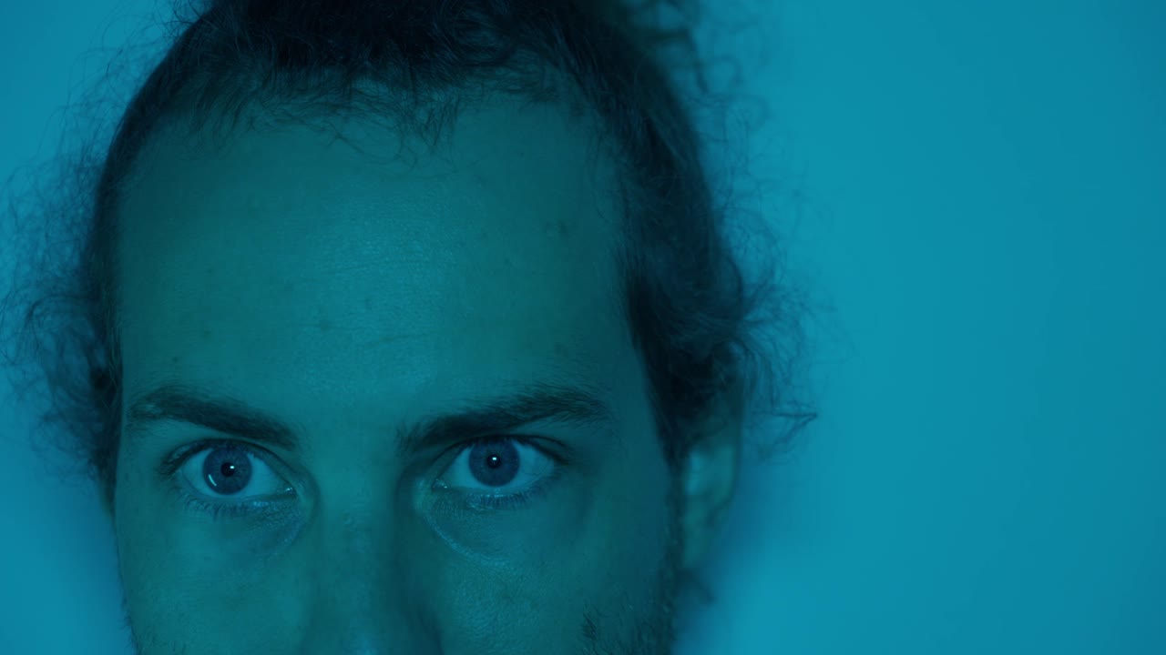 Close-up of man with eyes wide open under blue light raising head and blinking, peaceful, relaxed, soft atmospheric tone