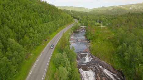 campervan driving along scenic mountain road by winding river in norway, aerial