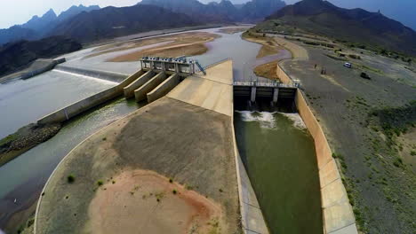 Aerial-view-of-spillway-of-a-dam,-Beautiful-majestic-mountains-in-the-back-of-the-dam