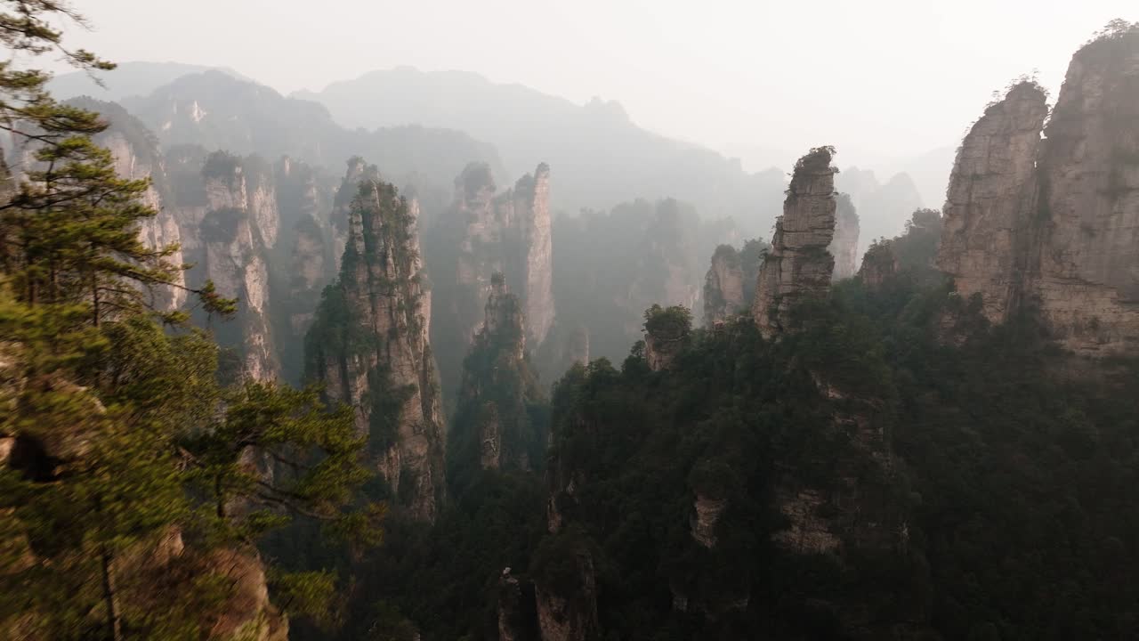 Aerial view of towering stone pinnacles rising from dense forest beneath a hazy mountain skyline in Zhangjiajie National Park