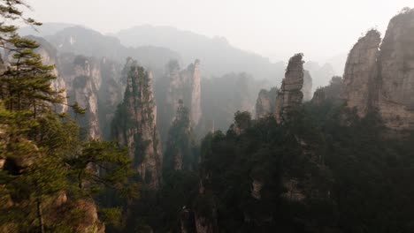 aerial view of towering stone pinnacles rising from dense forest beneath a hazy mountain skyline in zhangjiajie national park