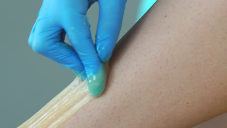primer plano en el salón de belleza maestro en guantes haciendo el procedimiento para eliminar el vello en las piernas con una mezcla de azúcar