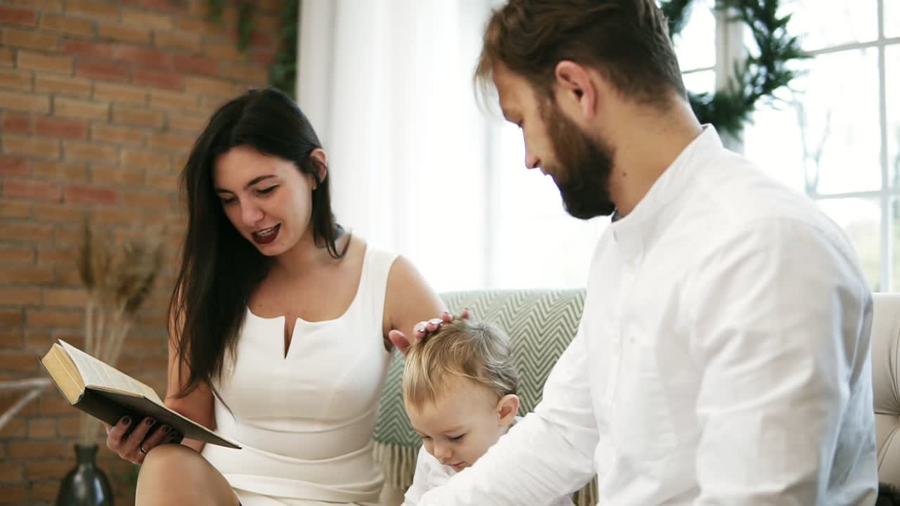 madre joven leyendo un libro para su hijo y su marido. familia leyendo un cuento navideño mientras está sentado junto al árbol de navidad. niño feliz