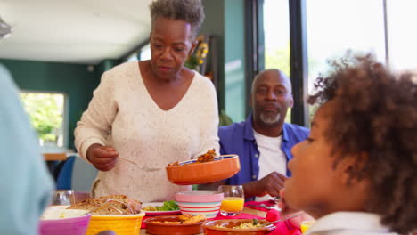 multi-generation family sitting around table at home enjoying meal together