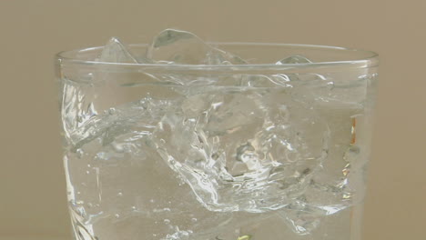 clear sparkling water poured over ice cubes into a clear glass tumbler