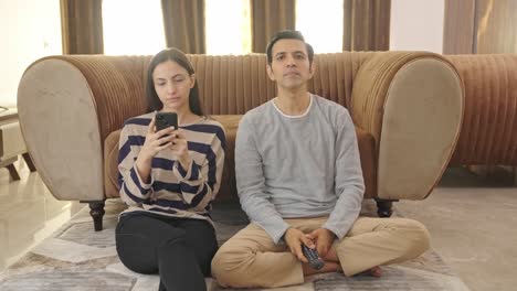 indian husband watching tv and wife is busy on phone