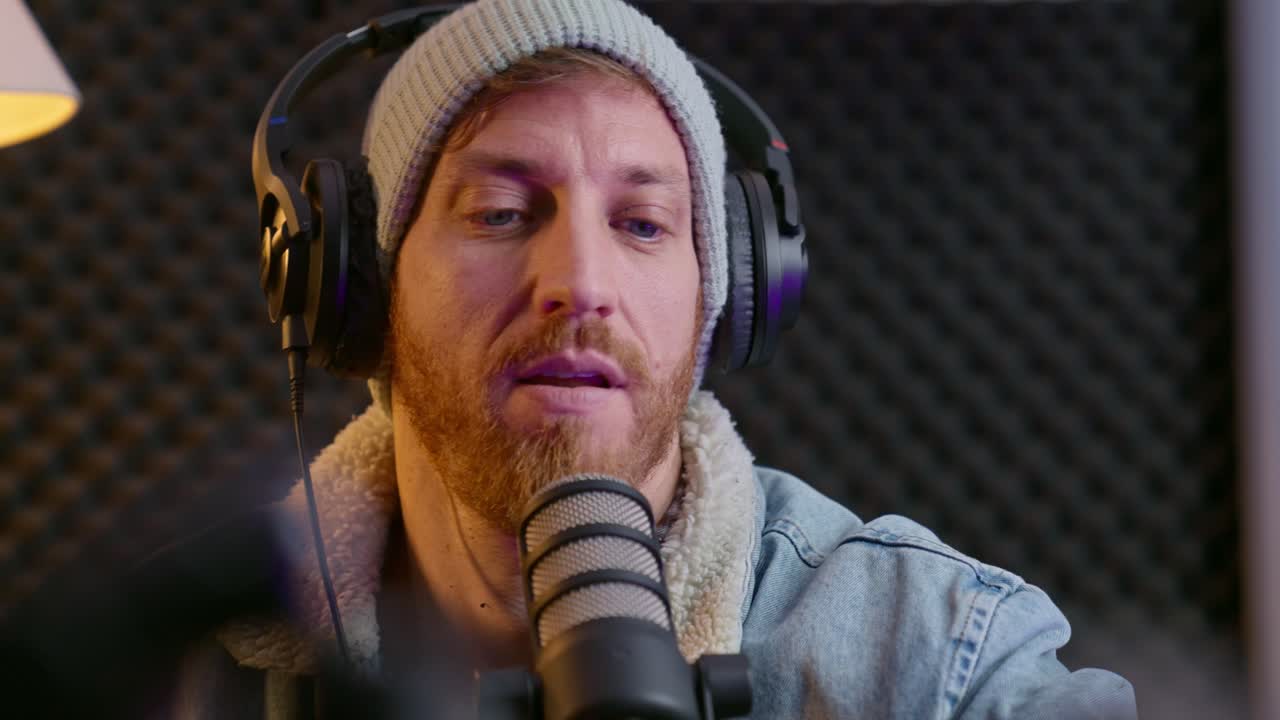podcaster tocando el micrófono mientras realiza una comprobación de sonido en un estudio de podcast profesional. la habitación cuenta con una configuración acogedora, auriculares, paredes de espuma acústica e iluminación cálida para una atmósfera moderna