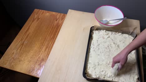 above static: woman slowly pouring flour from bowl over pie dough