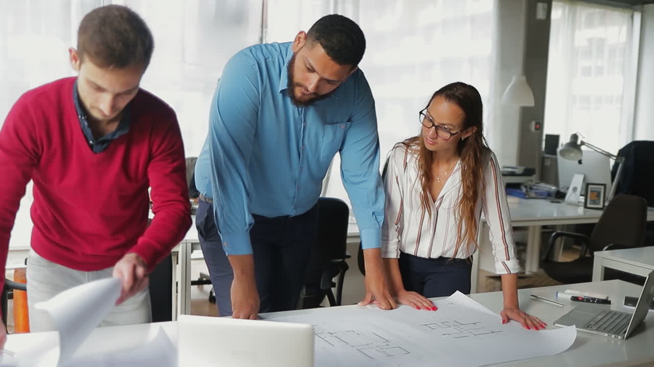 arquitectos confiados concentrados trabajando con planos en la oficina.