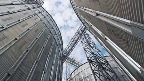 large grain elevators. silver granary for storing crop. metal grain terminals outdoors. agricultural warehouses. view from below