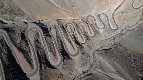 Aerial-overhead-orbit-of-the-cuesta-caracoles-road,-border-between-Chile-and-Argentina,-cargo-trucks-passing-through-the-curves